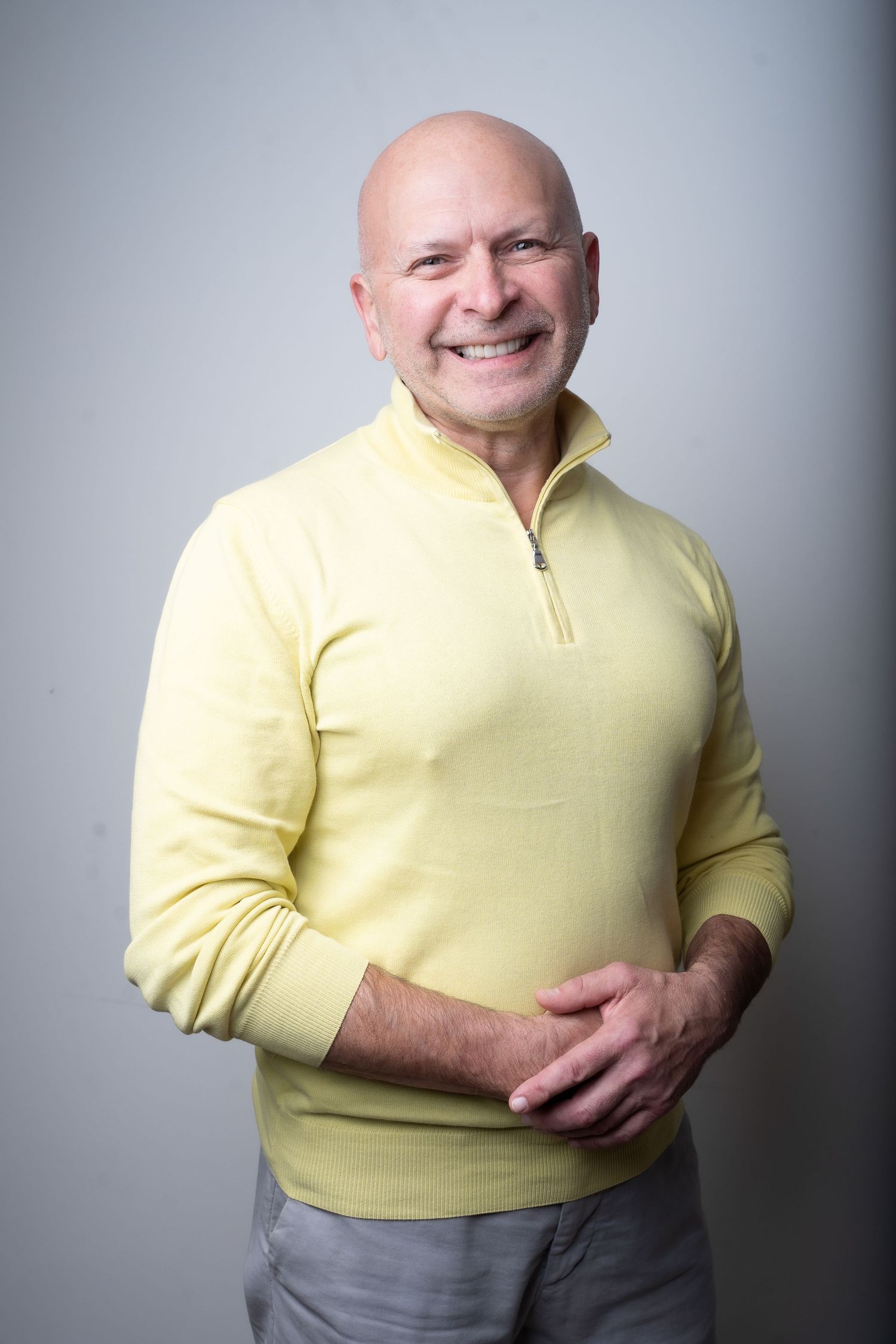 A person wearing a yellow quarter-zip sweater poses against a gray background in a series of casual portraits.