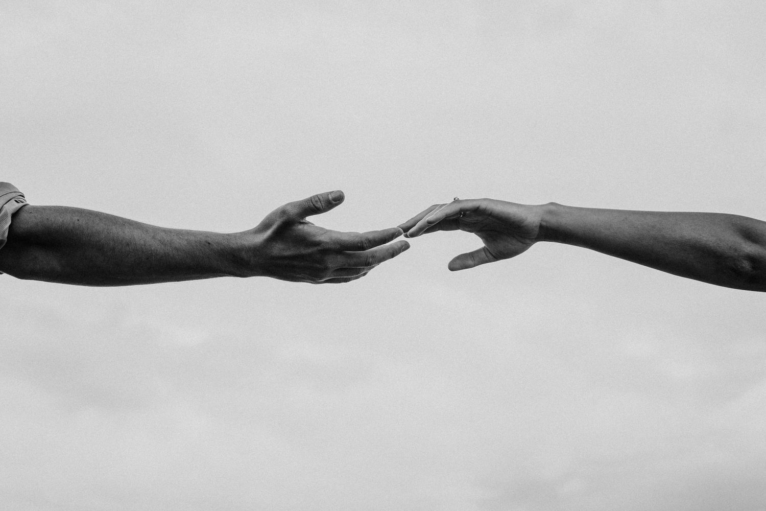 A black and white image of two hands reaching out and touching every so gently. A vision of romance and yearning passion.
