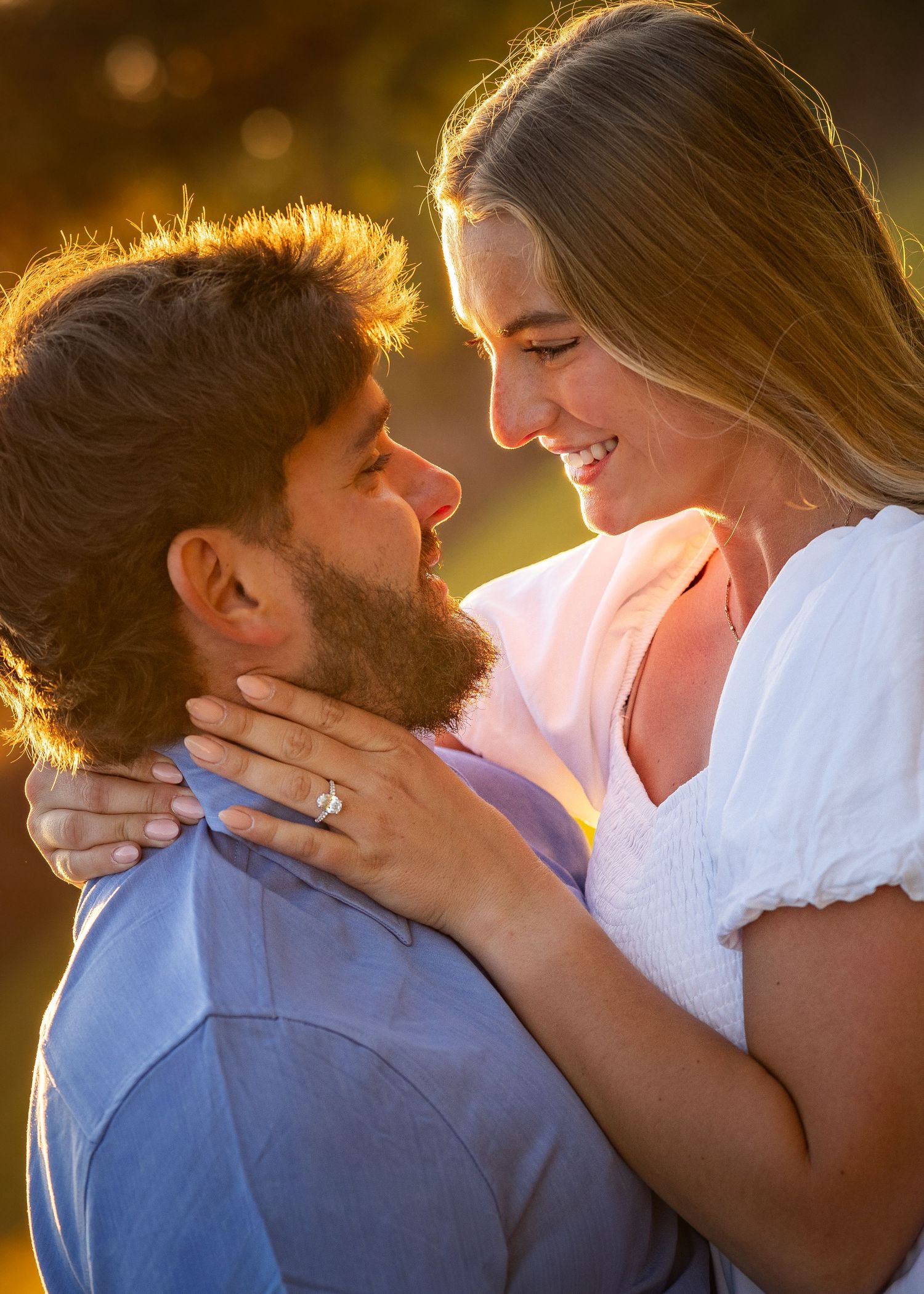 Joyful couple nearly kissing in warm golden hour sunlight during romantic engagement photo session.