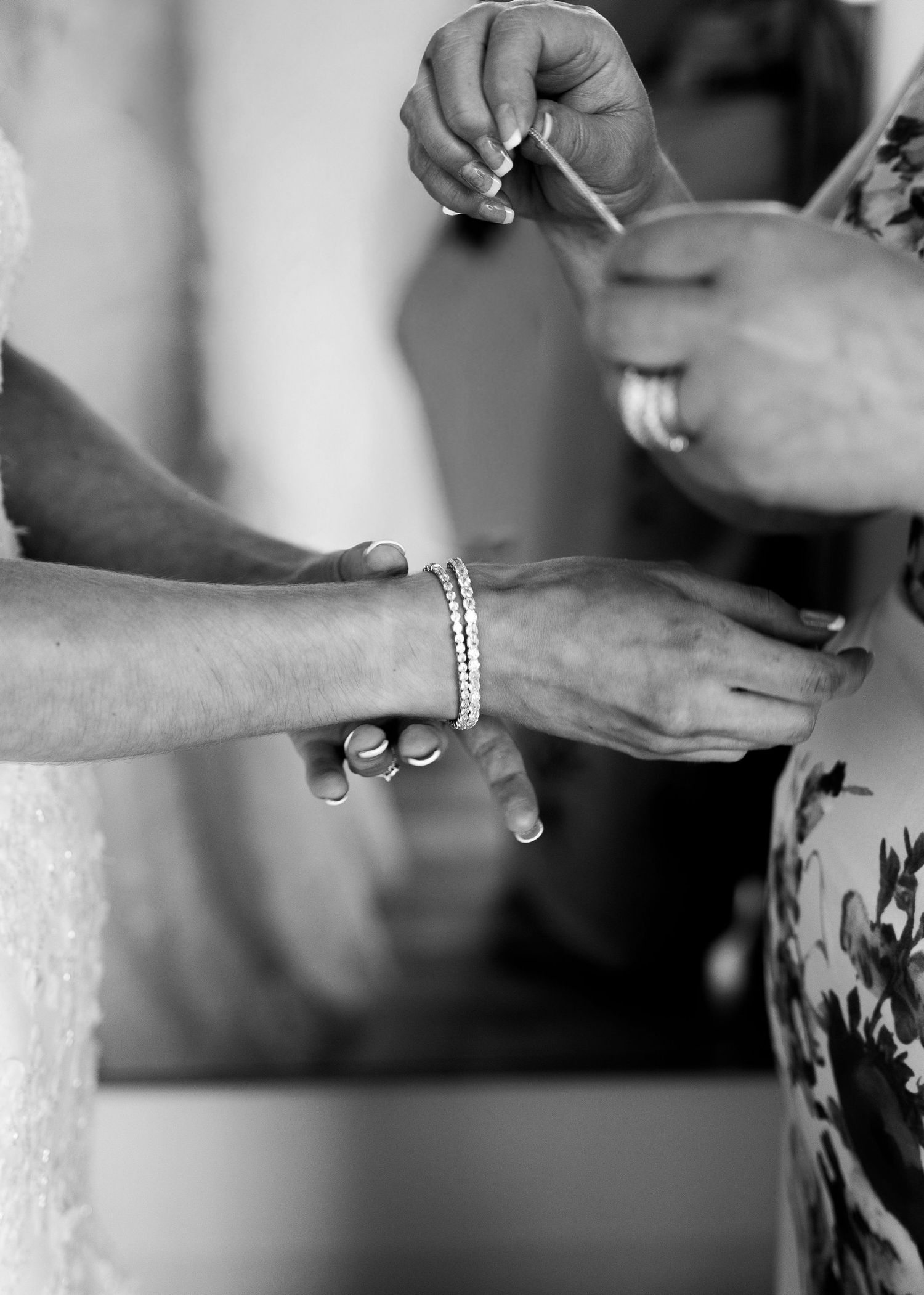 Close-up black and white photo of hands fastening bride's bracelet during wedding day preparations.