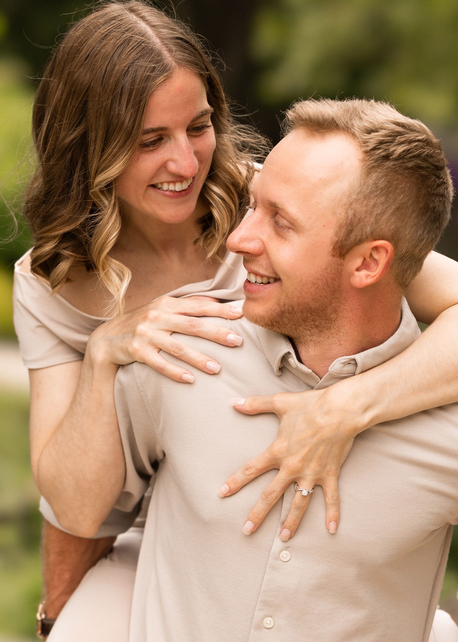 Happy couple sharing a joyful embrace outdoors, woman wrapping arms around mans neck showing engagement ring.
