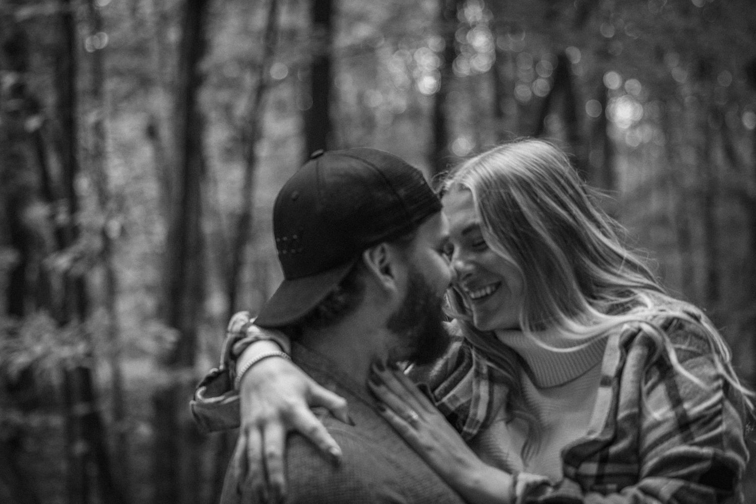 Couple embracing and smiling together in a black and white forest engagement photo.