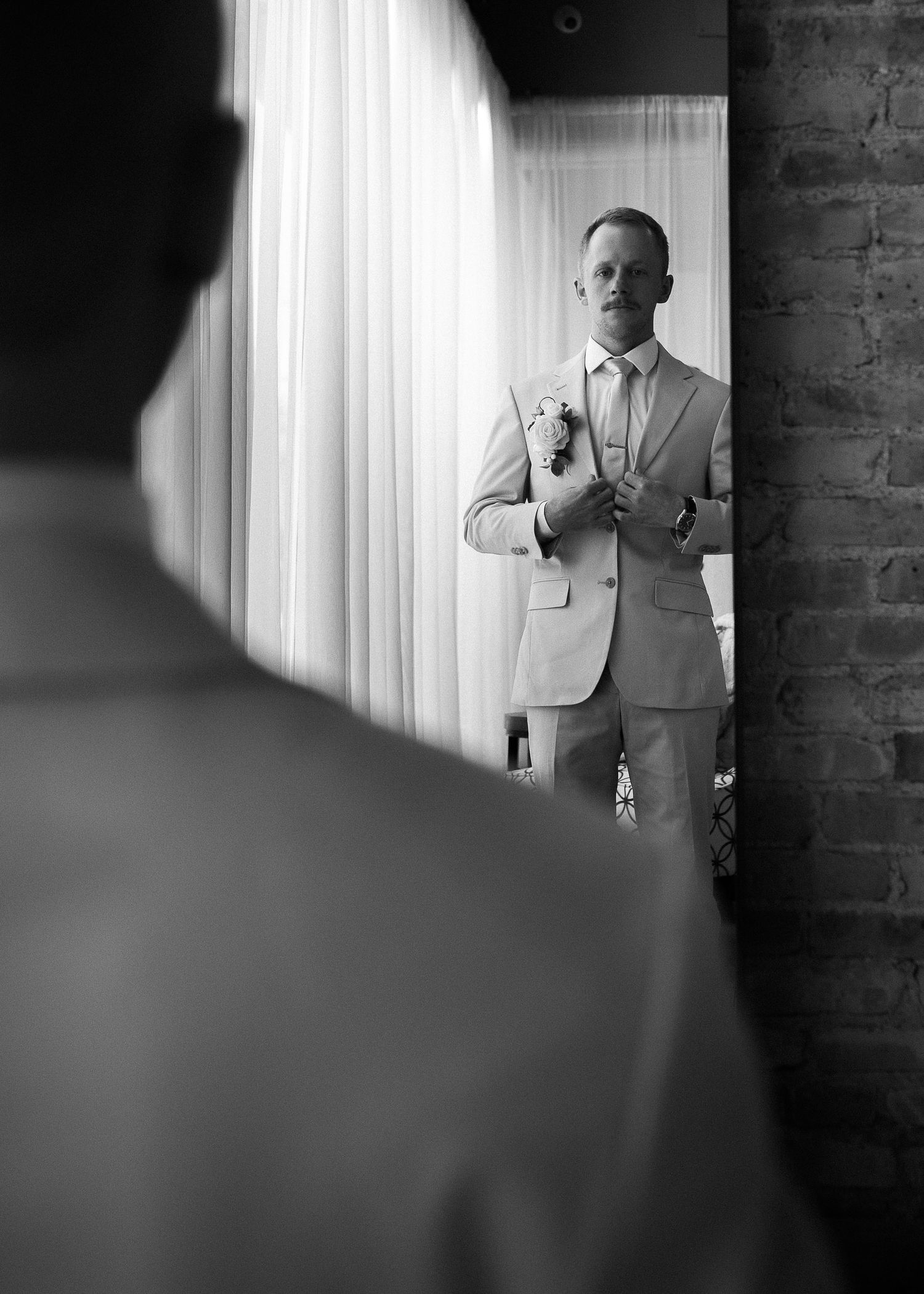 Dapper groom in tan suit adjusting cufflinks while preparing for wedding, captured in black and white.