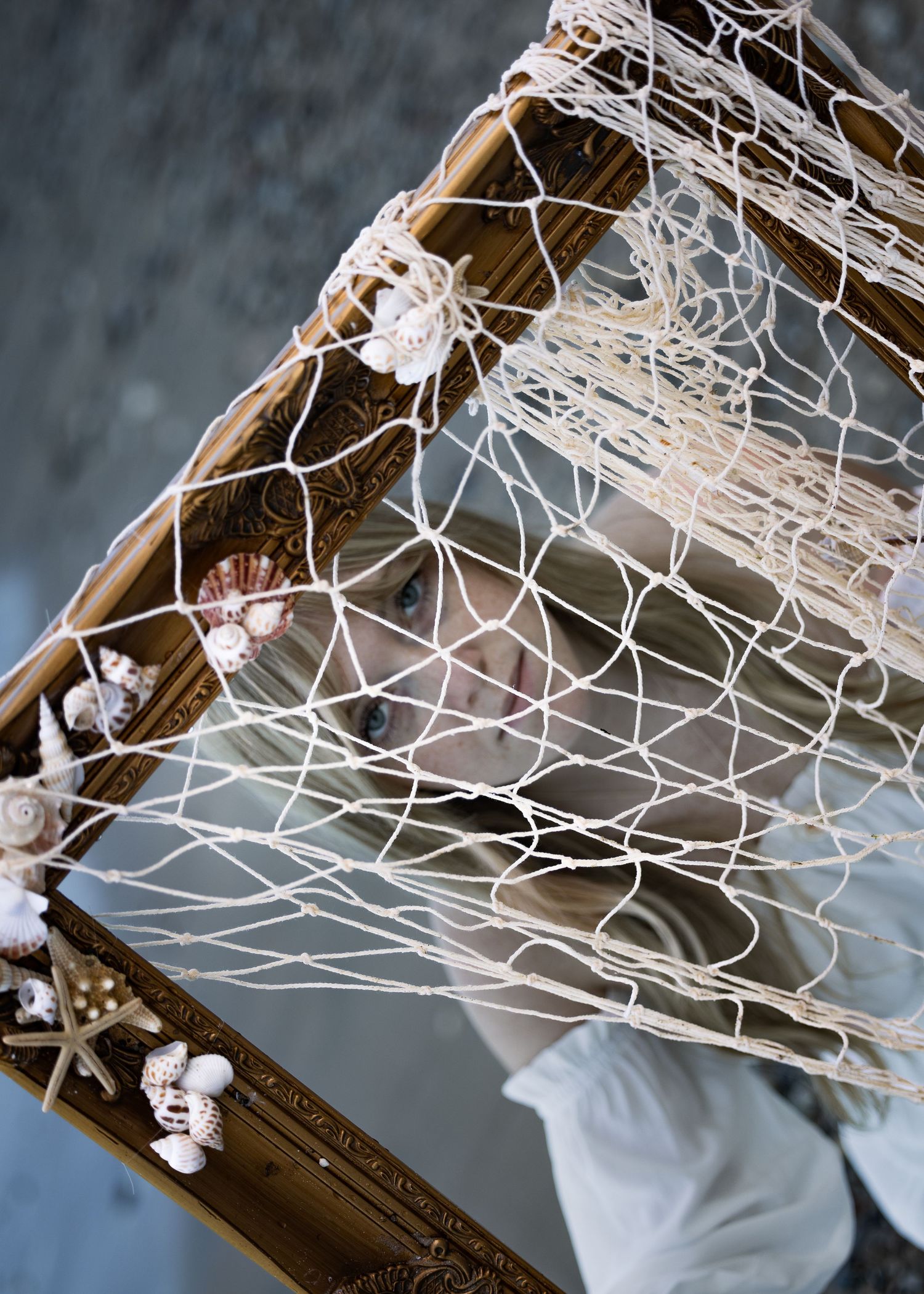 Decorative gold mirror frame adorned with seashells and draped white fishing net in a coastal nautical display.
