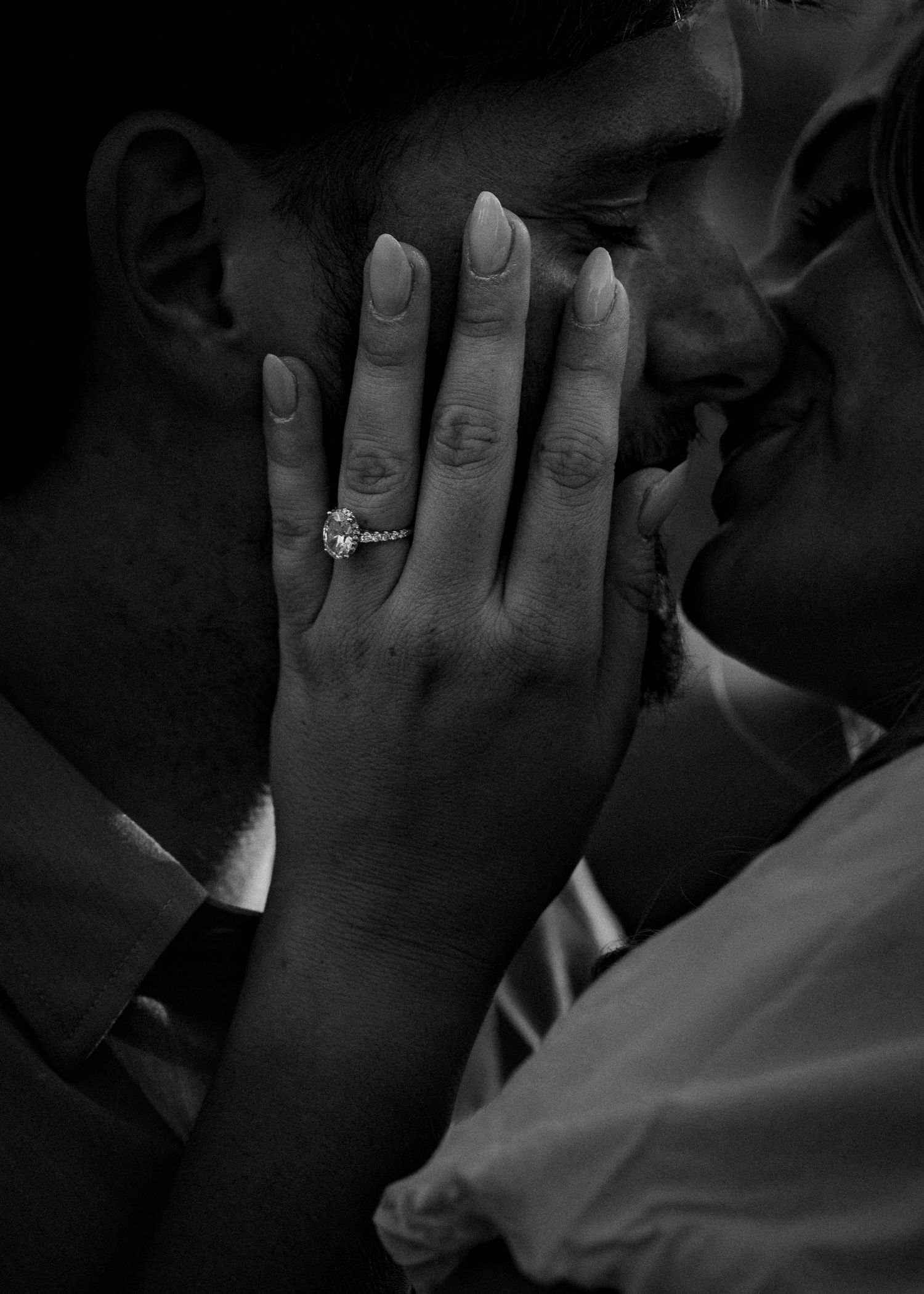 Black and white close-up of couple kissing with engagement ring prominently displayed on her hand.