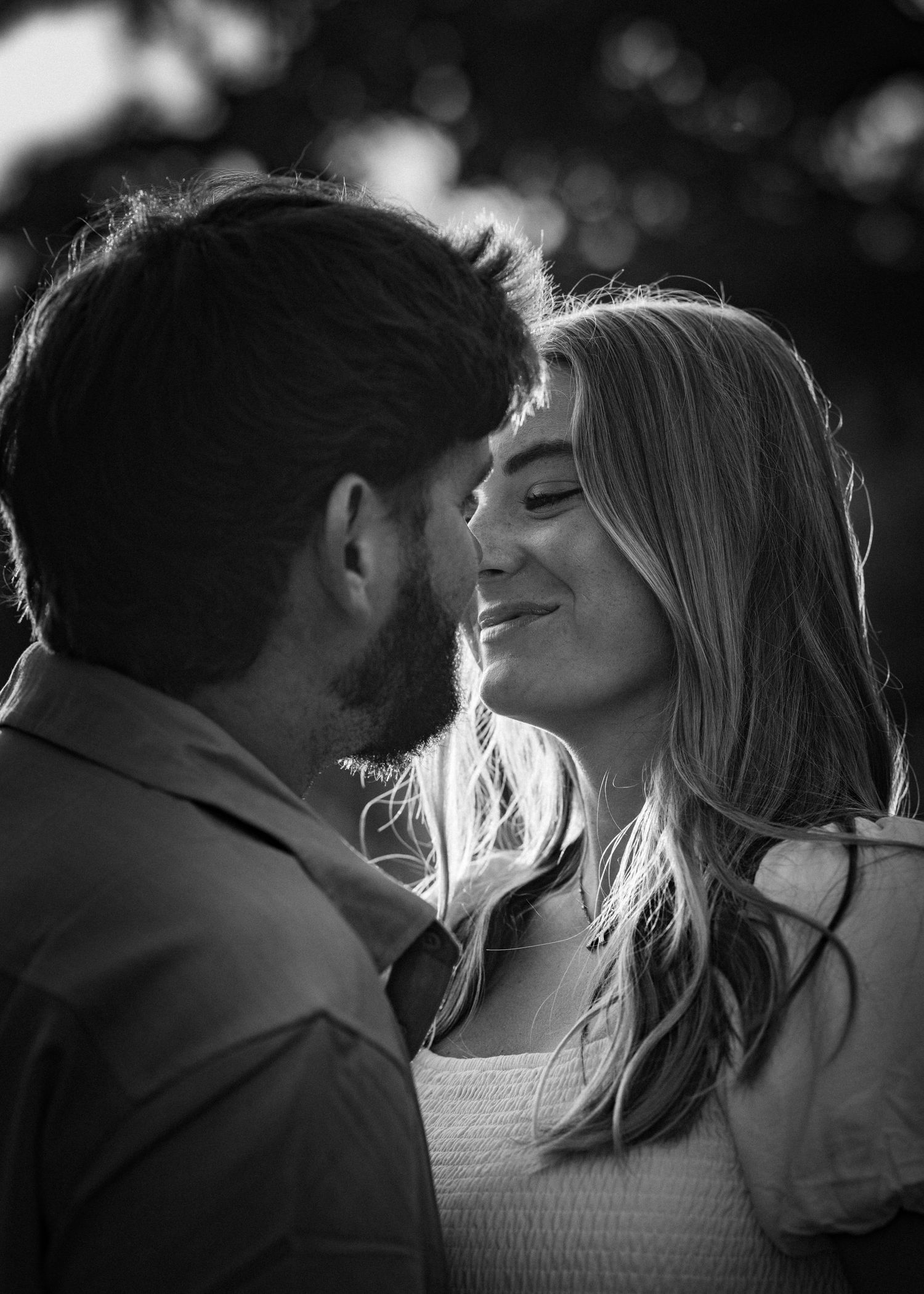 Black and white photo of a couple sharing a tender moment, nearly kissing outdoors.