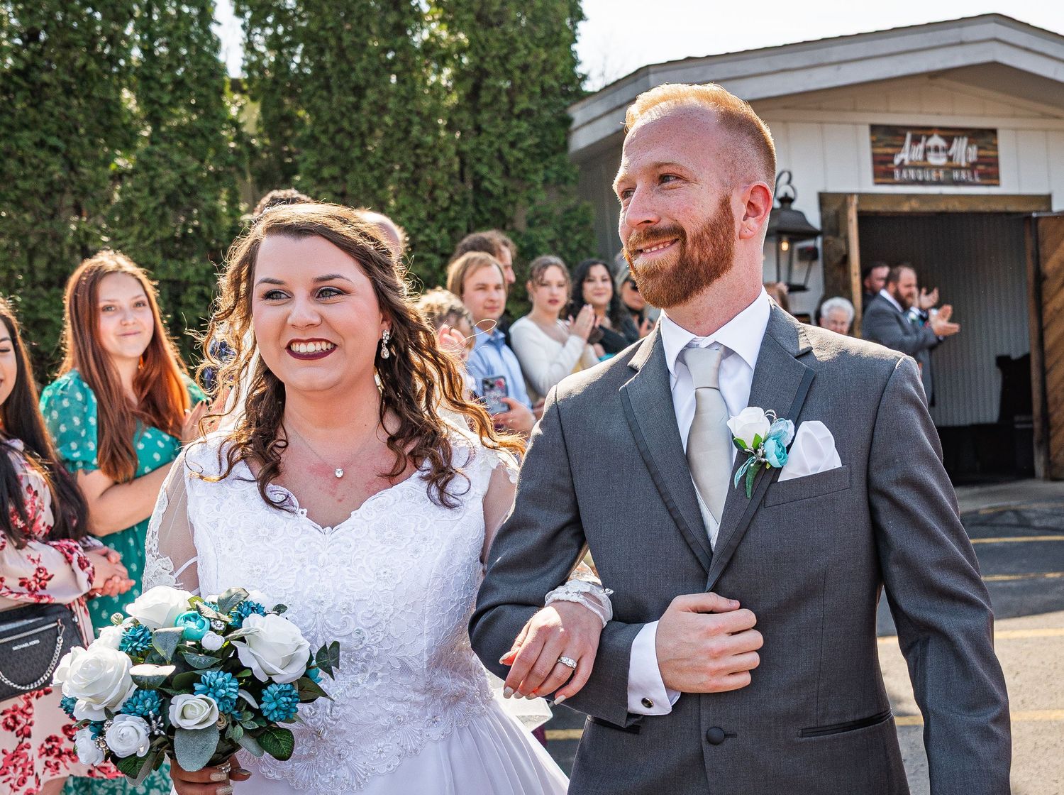 Bride and groom smiling at each other under rustic wooden pergola with string lights at outdoor wedding venue.
