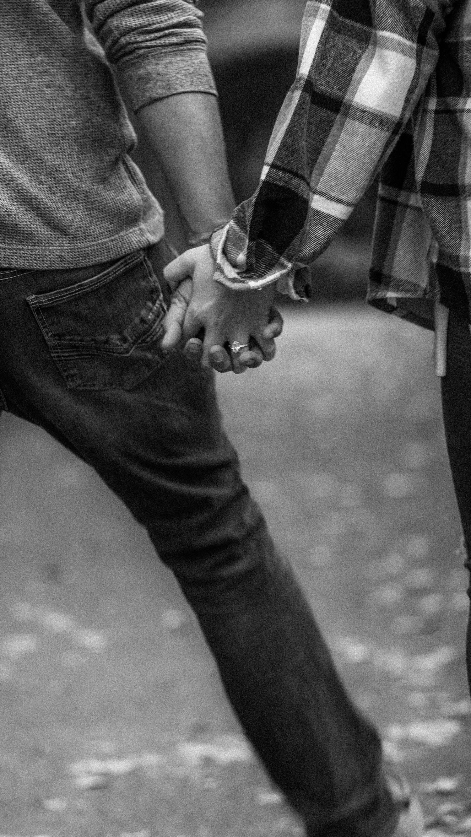 Close-up black and white photo of couple holding hands showing engagement ring.