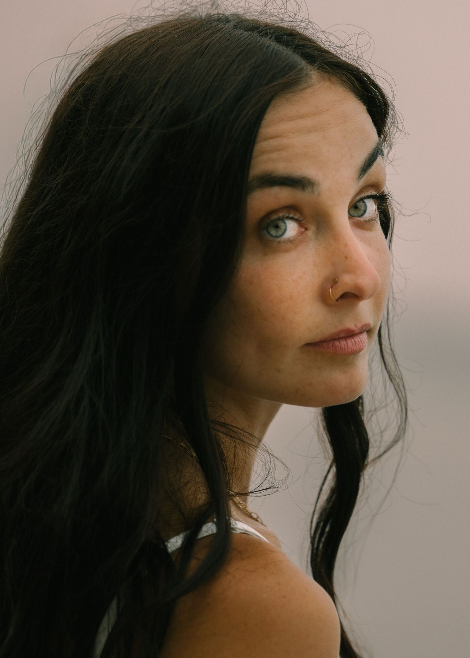 Young woman with long dark hair and green eyes gazing over her shoulder in a close-up portrait photo.