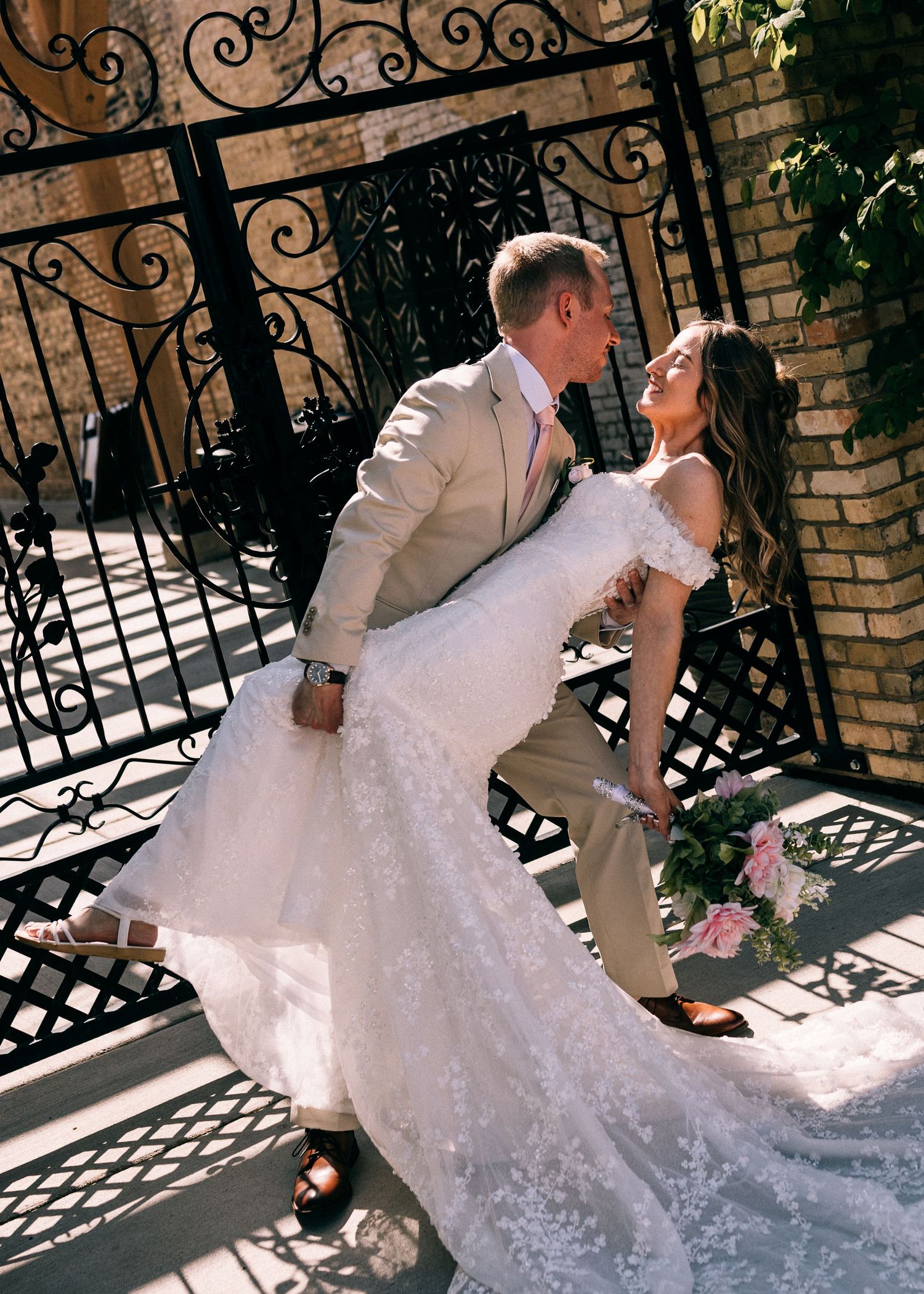 Bride and groom sharing romantic dip kiss in front of ornate iron gates at outdoor venue.