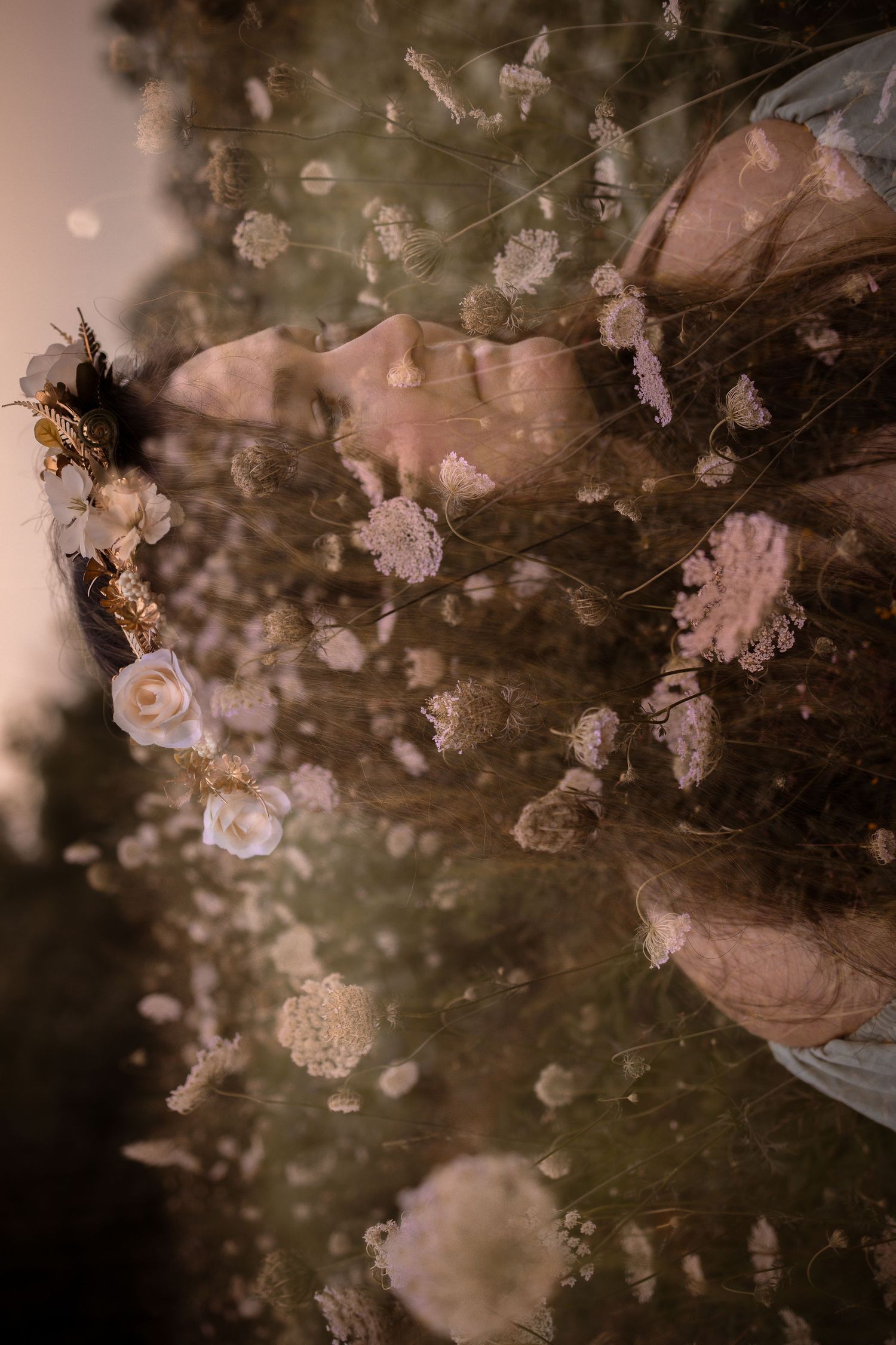 Double exposure portrait of a woman with floral crown merged with blooming wildflowers in soft dreamy light.