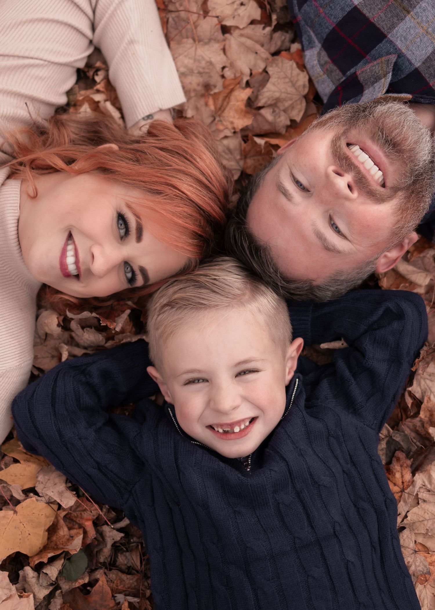 Aerial view of smiling family lying together in a bed of golden autumn leaves.