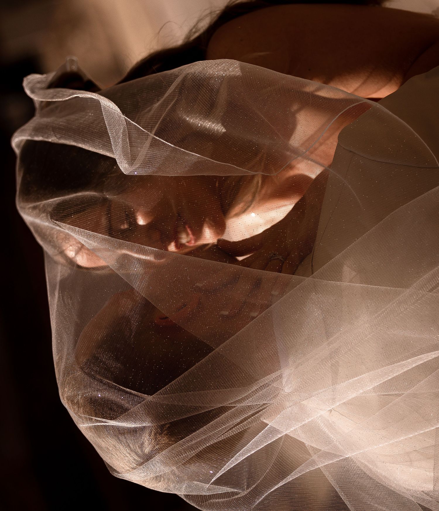 A person draped in sheer white fabric, with hands visible through the translucent veil in dramatic lighting.
