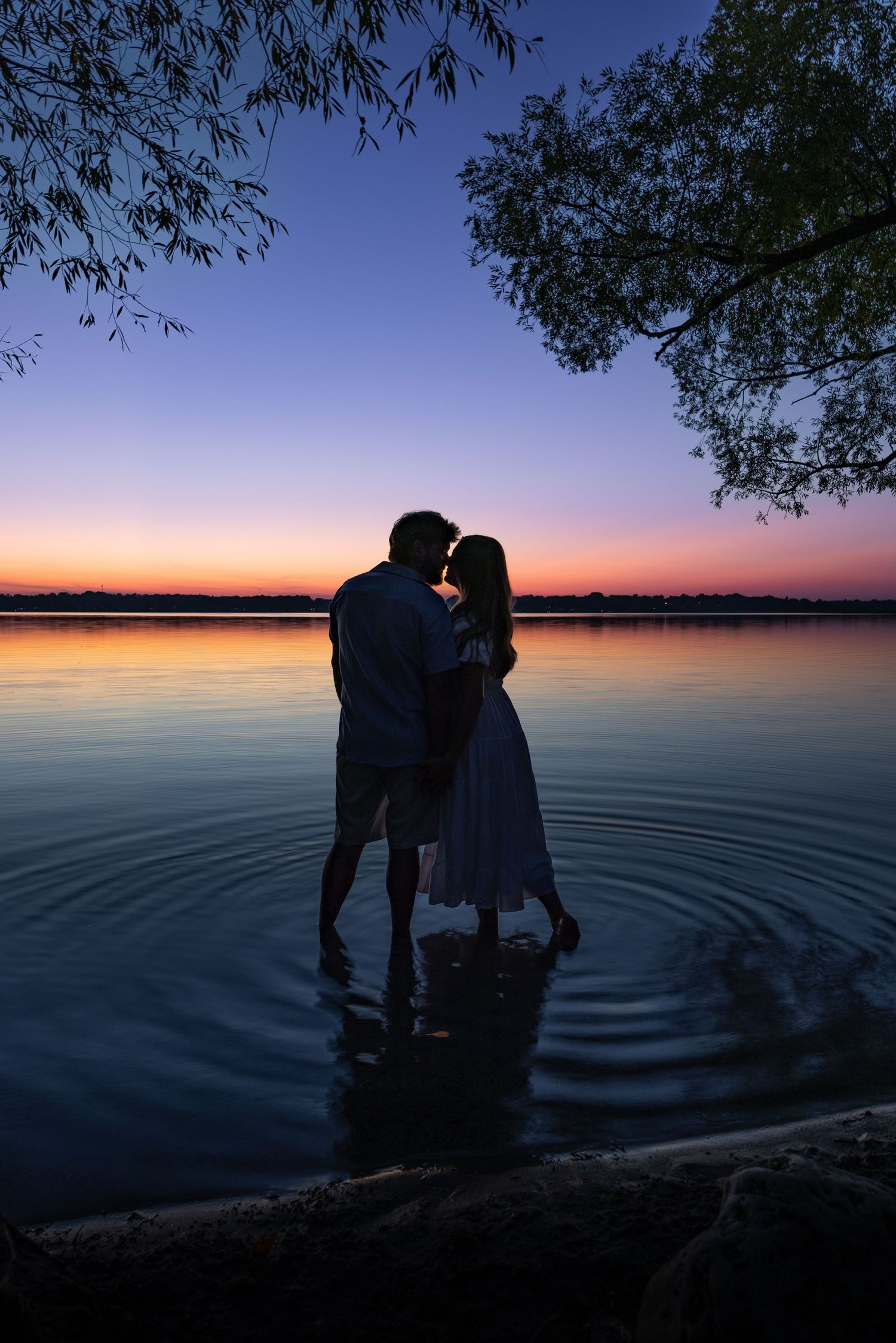 Romantic couple silhouette kissing in lake water at stunning purple and orange sunset twilight.
