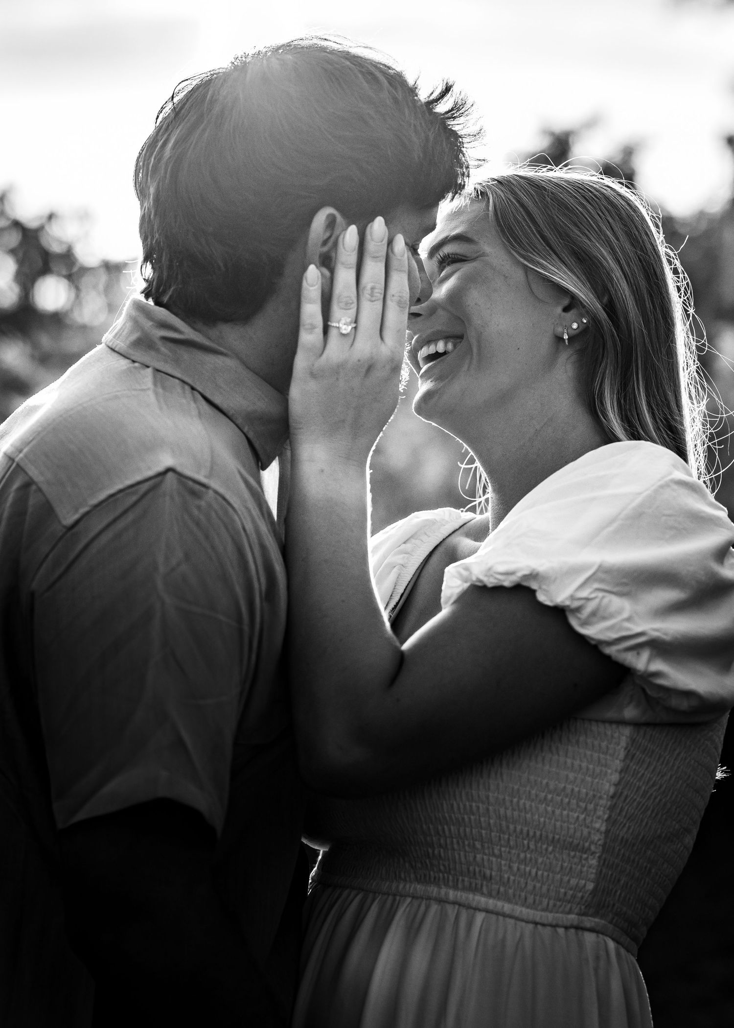 Black and white photo of a smiling couple sharing a close romantic moment outdoors.
