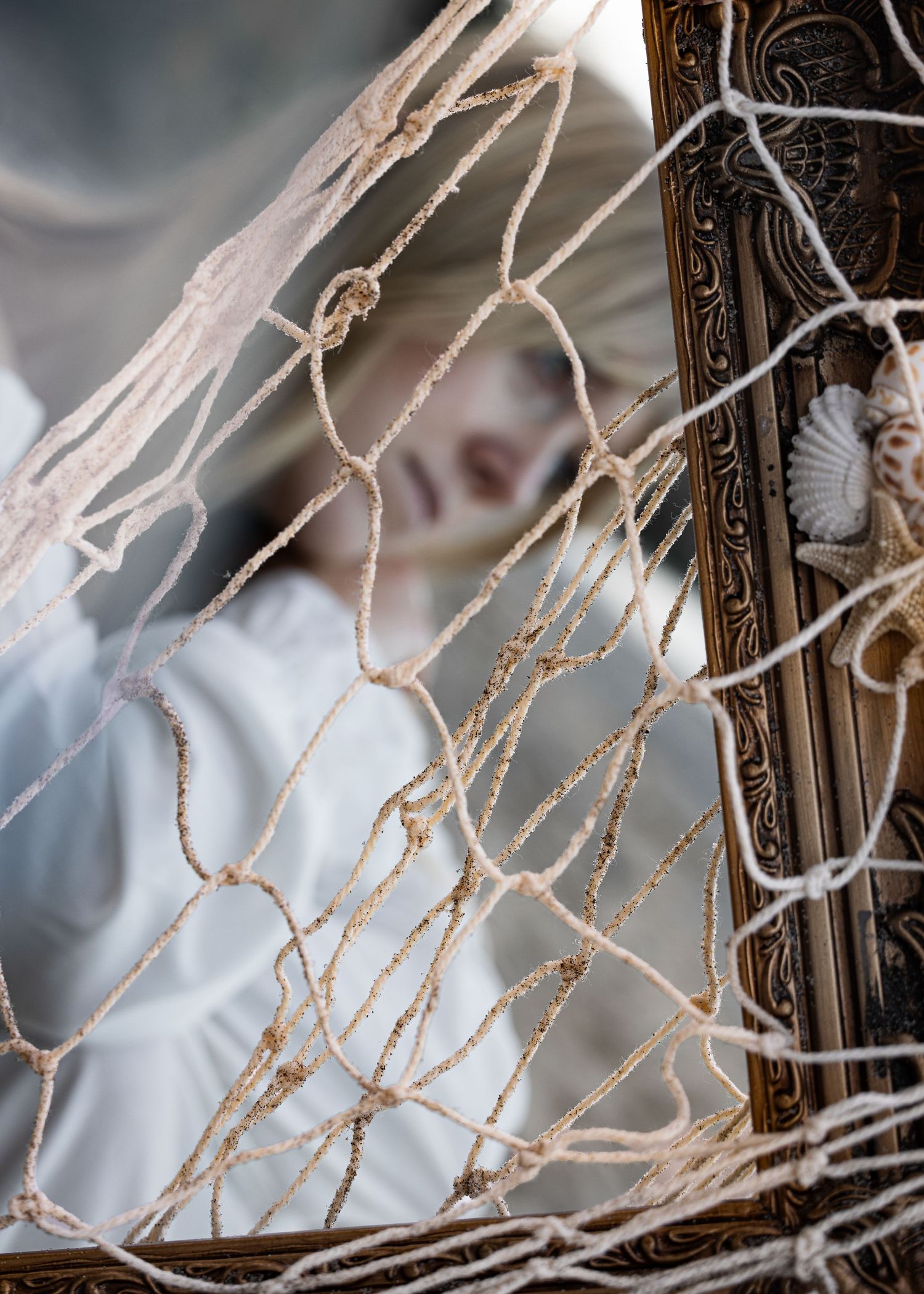 A decorative ornate mirror reflects a blurred figure through a tangled fishing net in the foreground.