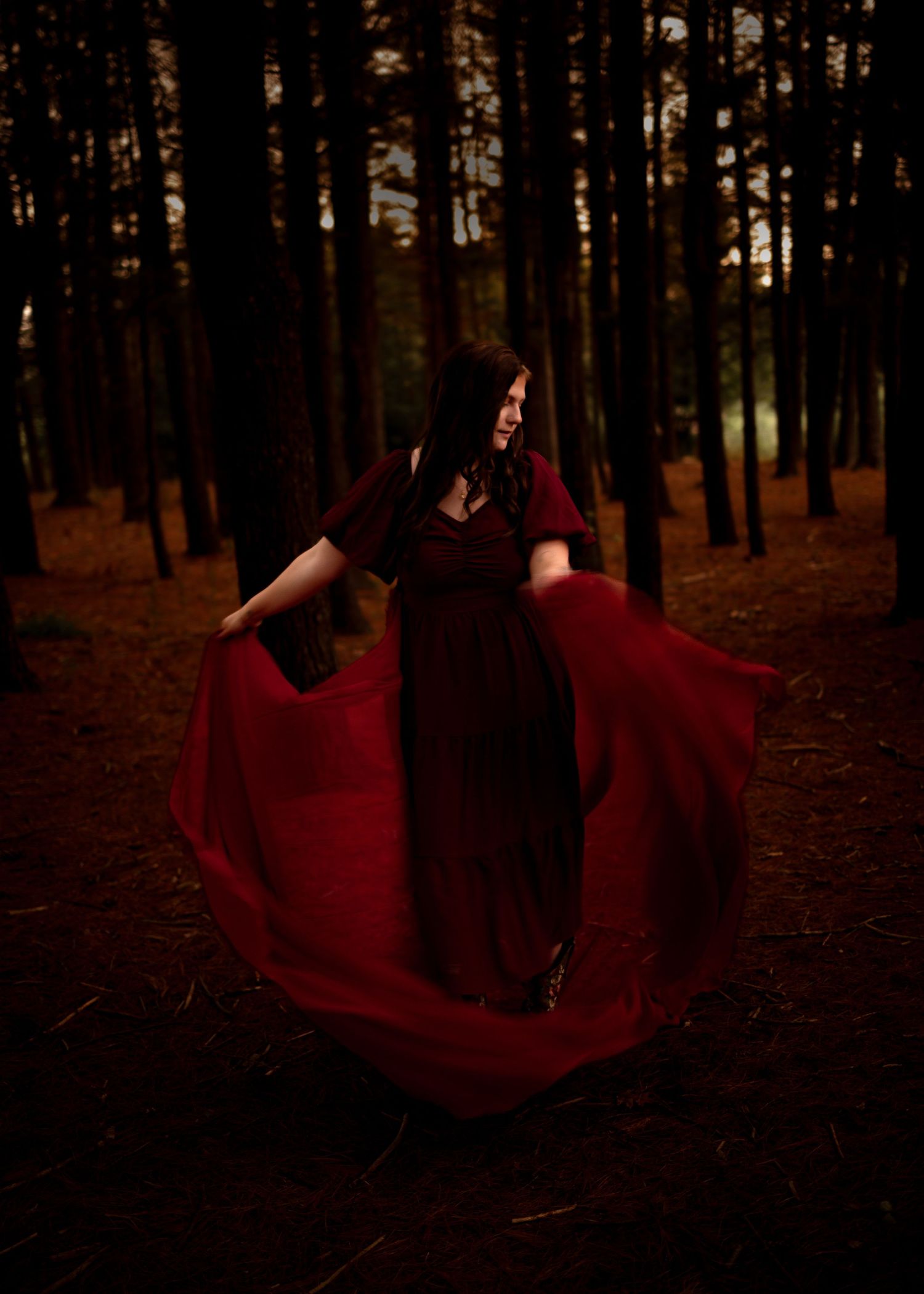 Woman in flowing red gown dancing dramatically in a dark forest, creating a mystical and ethereal atmosphere.
