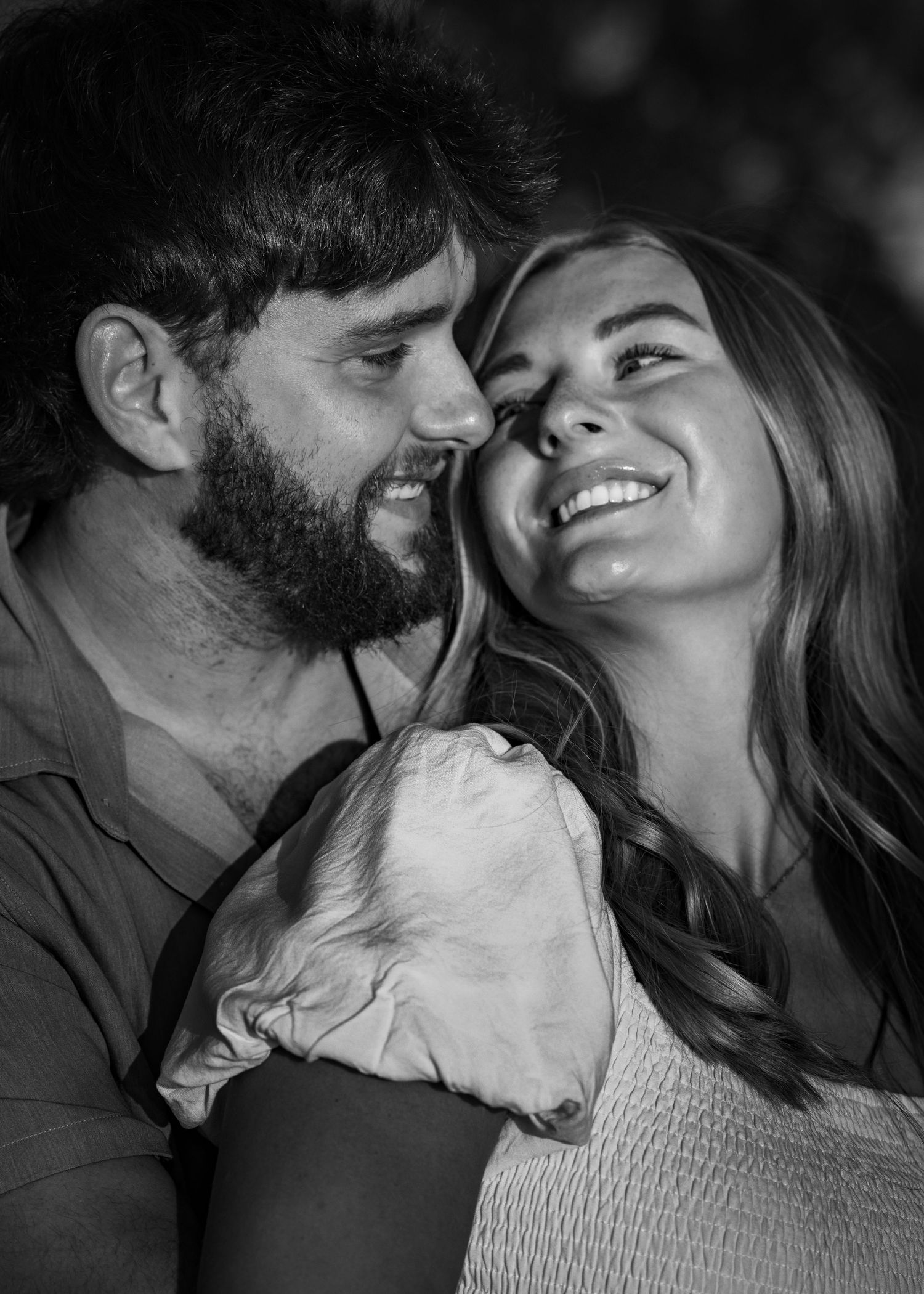 Smiling couple in an intimate black and white engagement portrait outdoors.