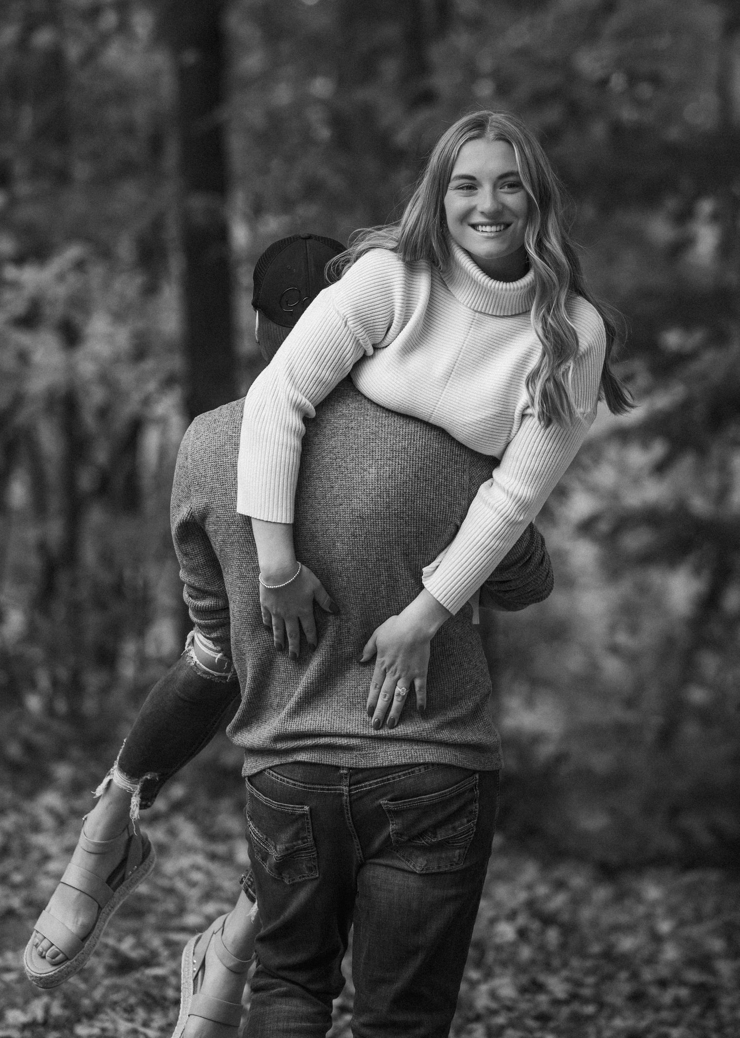 Woman laughing while getting a piggyback ride in autumn forest engagement photo.