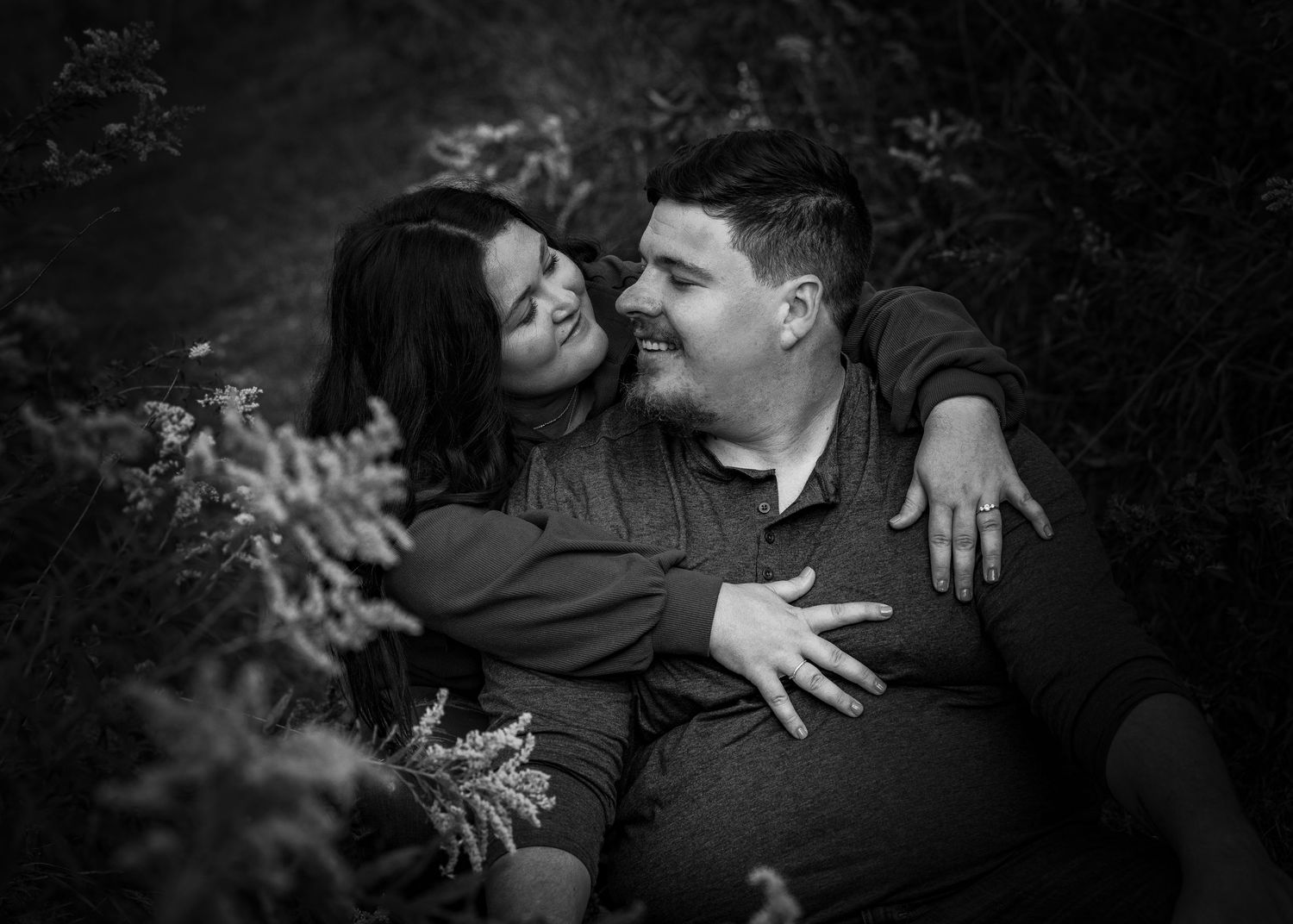 Happy couple laughing together surrounded by wildflowers in black and white photo.