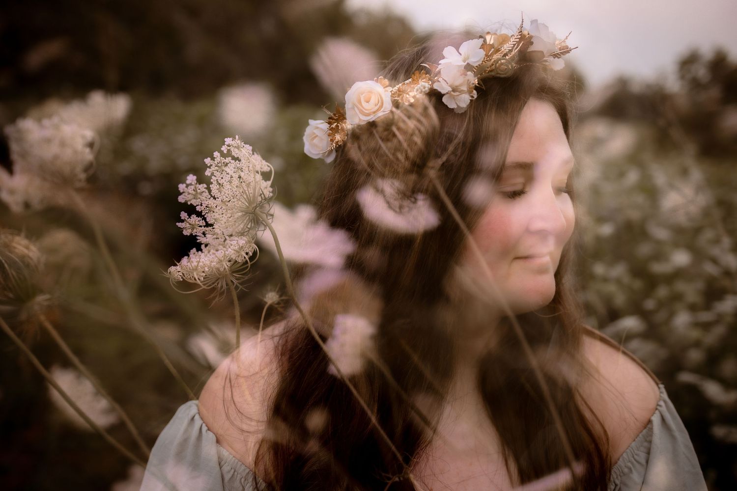Woman with floral crown smiling serenely among wildflowers in a dreamy, soft-focus outdoor portrait.