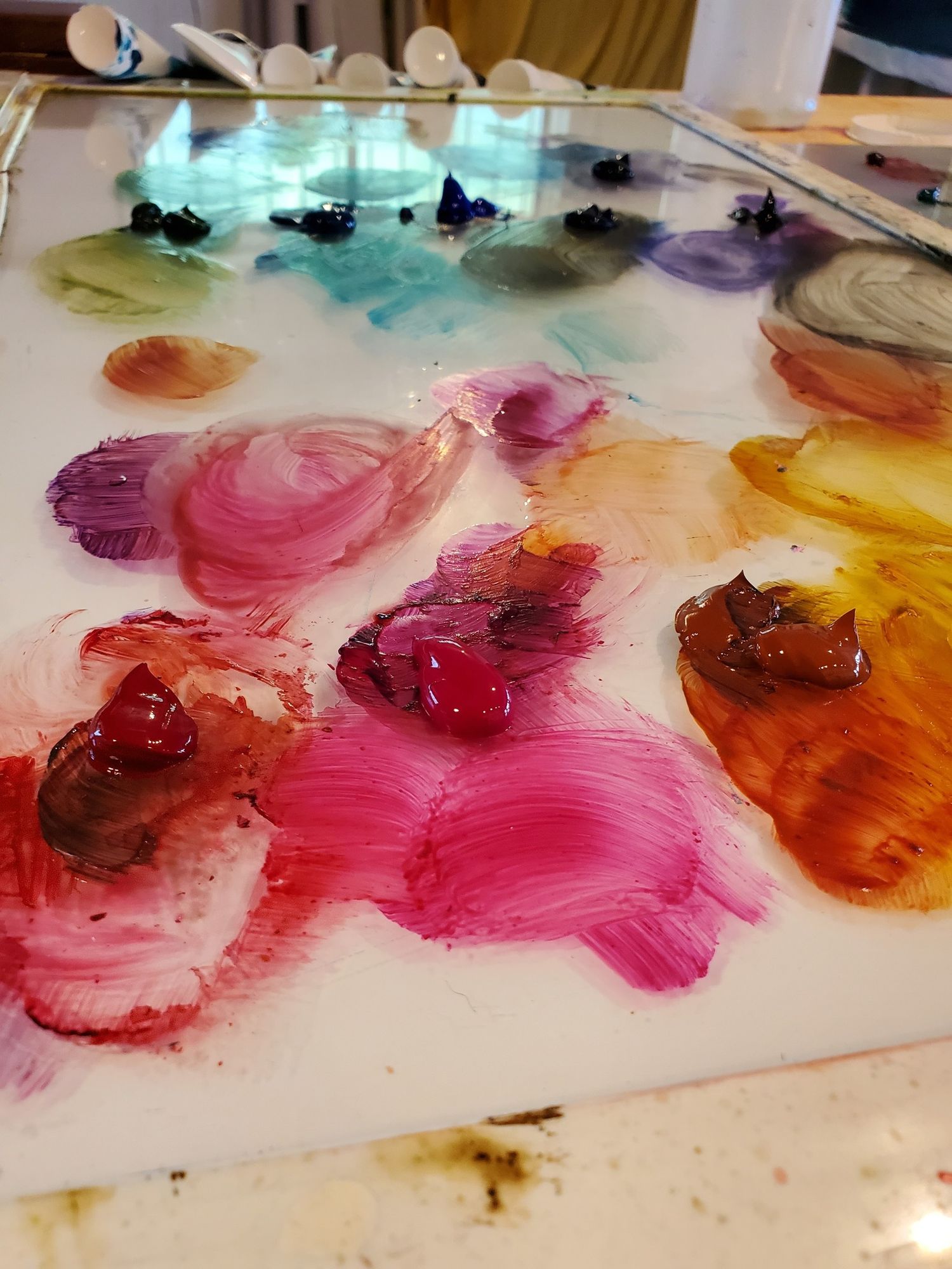 Close-up of a colorful artist paint palette with vibrant swirls of pink, purple, orange, and red oil paints.