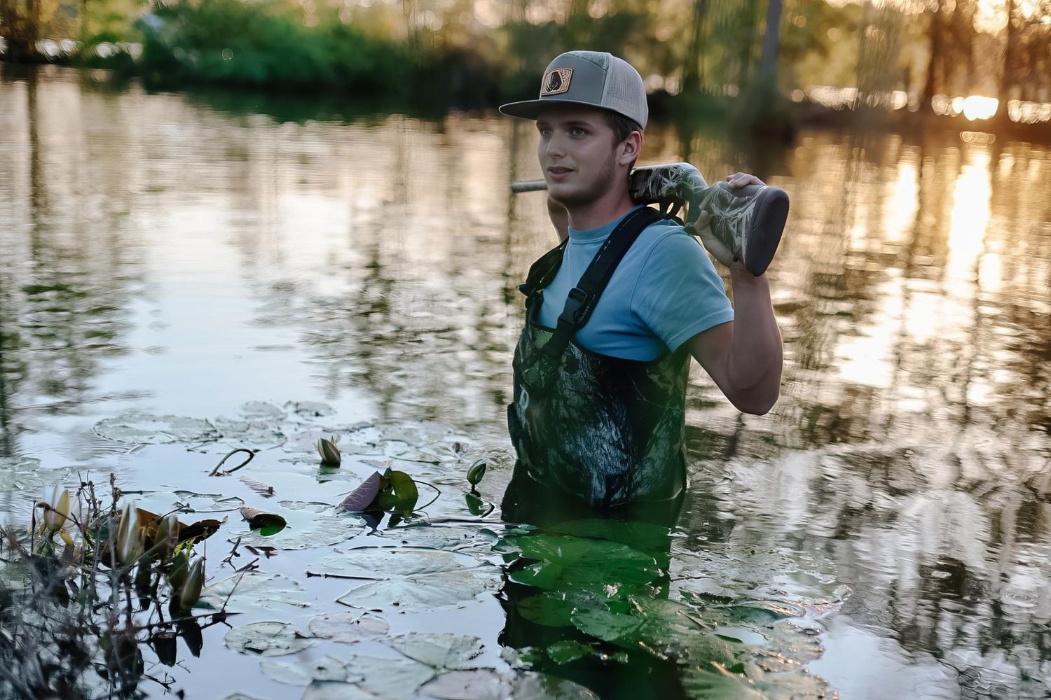 A person wearing a life vest wades through shallow water at sunset with reflective ripples around them.