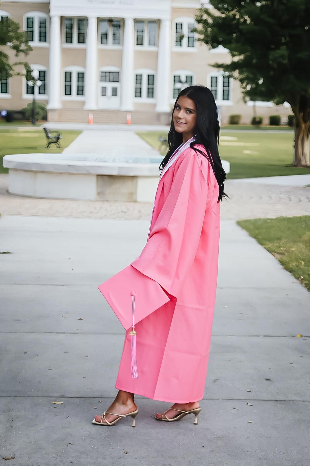 Coral pink graduation gown flows elegantly against academic building backdrop.