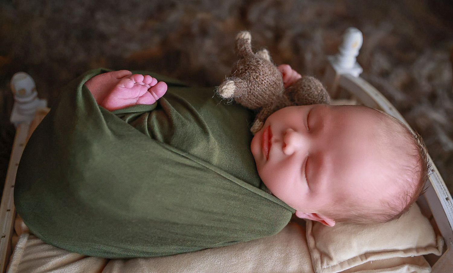 A sleeping newborn wrapped snugly in an olive green swaddle with a pink rose accent.