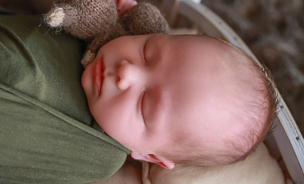 A sleeping infant wrapped in a soft green blanket rests peacefully.