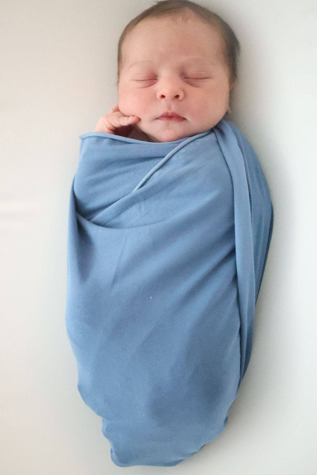Sleeping newborn baby swaddled in soft light blue blanket against white background.