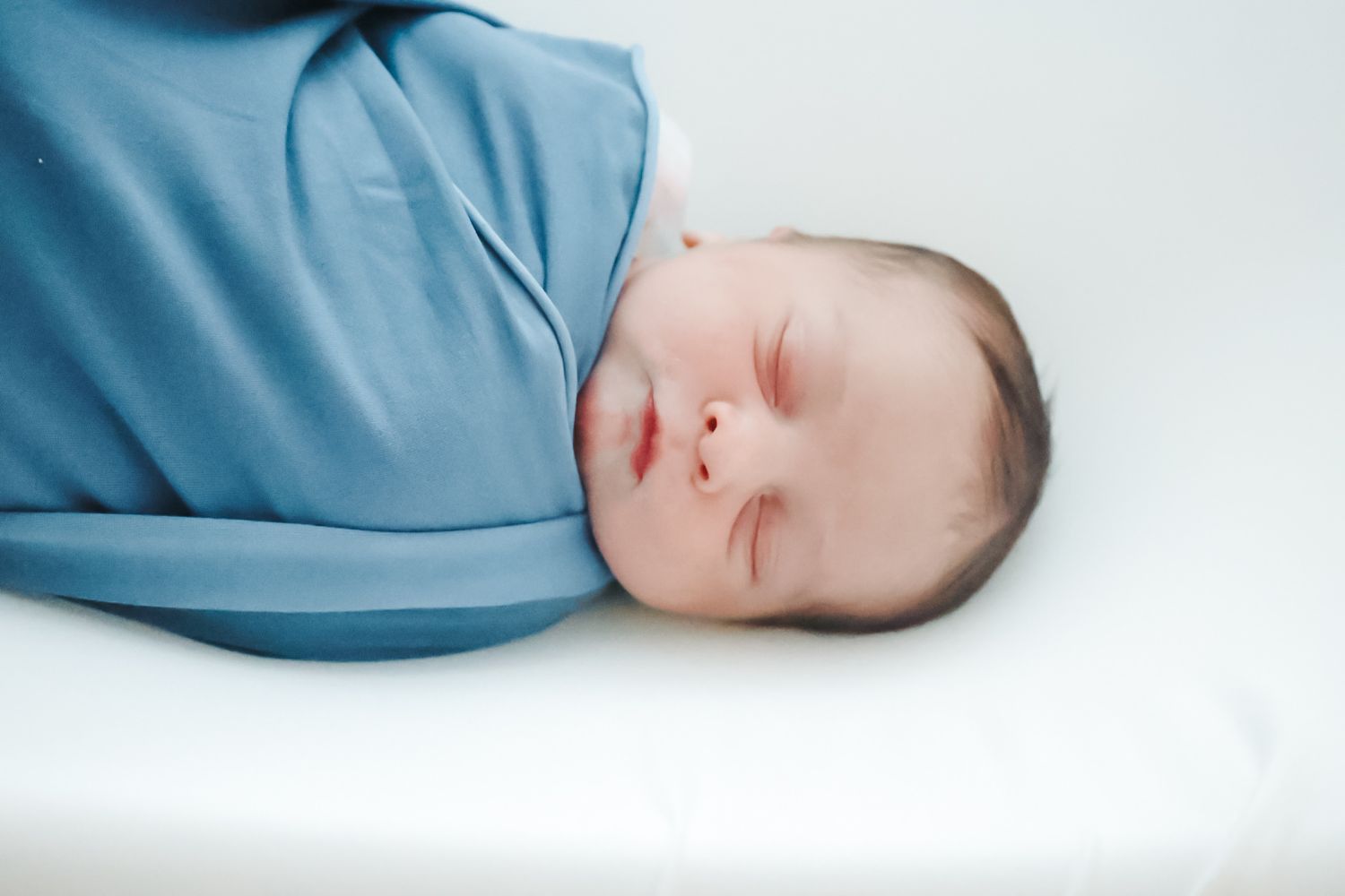 A sleeping baby in a light blue onesie rests peacefully on a white background.