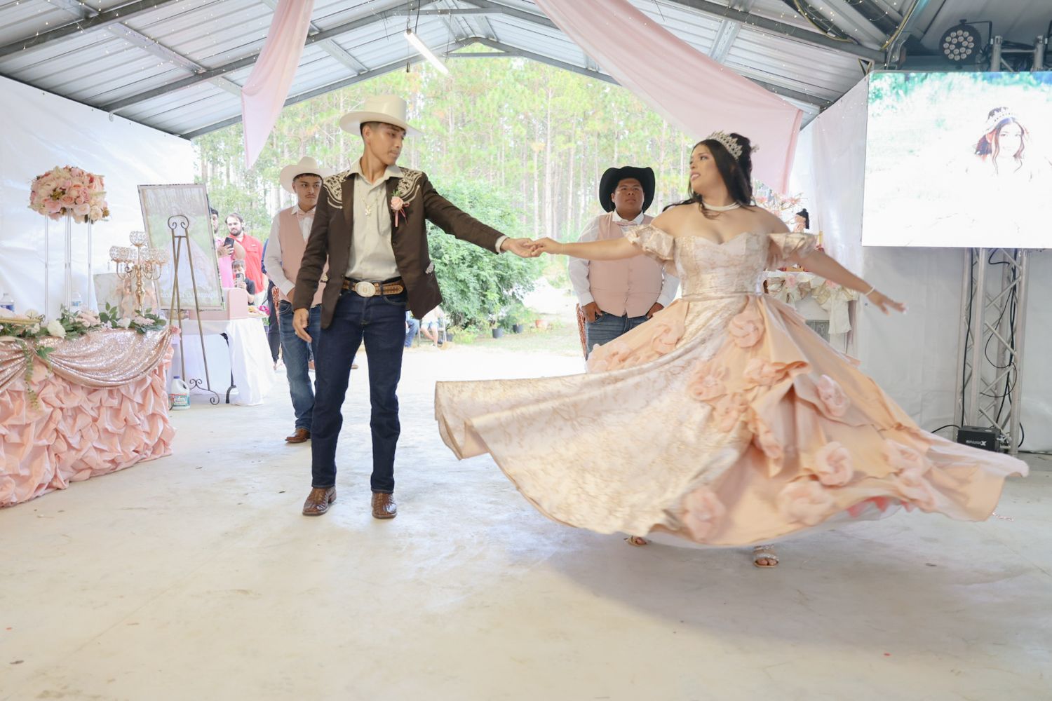 Young couple in Western attire dancing at a quinceañera celebration in a decorated outdoor venue.