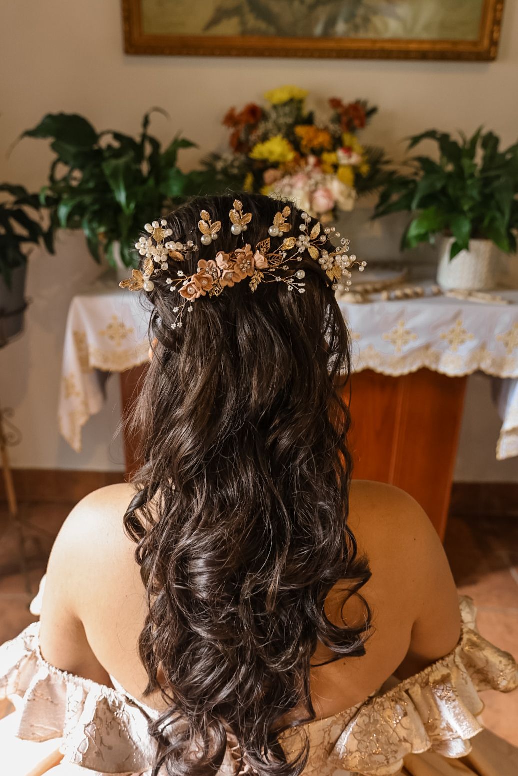 Back view of bride with long dark curly hair adorned with gold floral hair crown accessory.