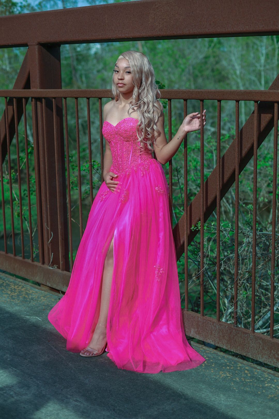 A stunning hot pink evening gown with sparkly details photographed on a wooden bridge surrounded by greenery.