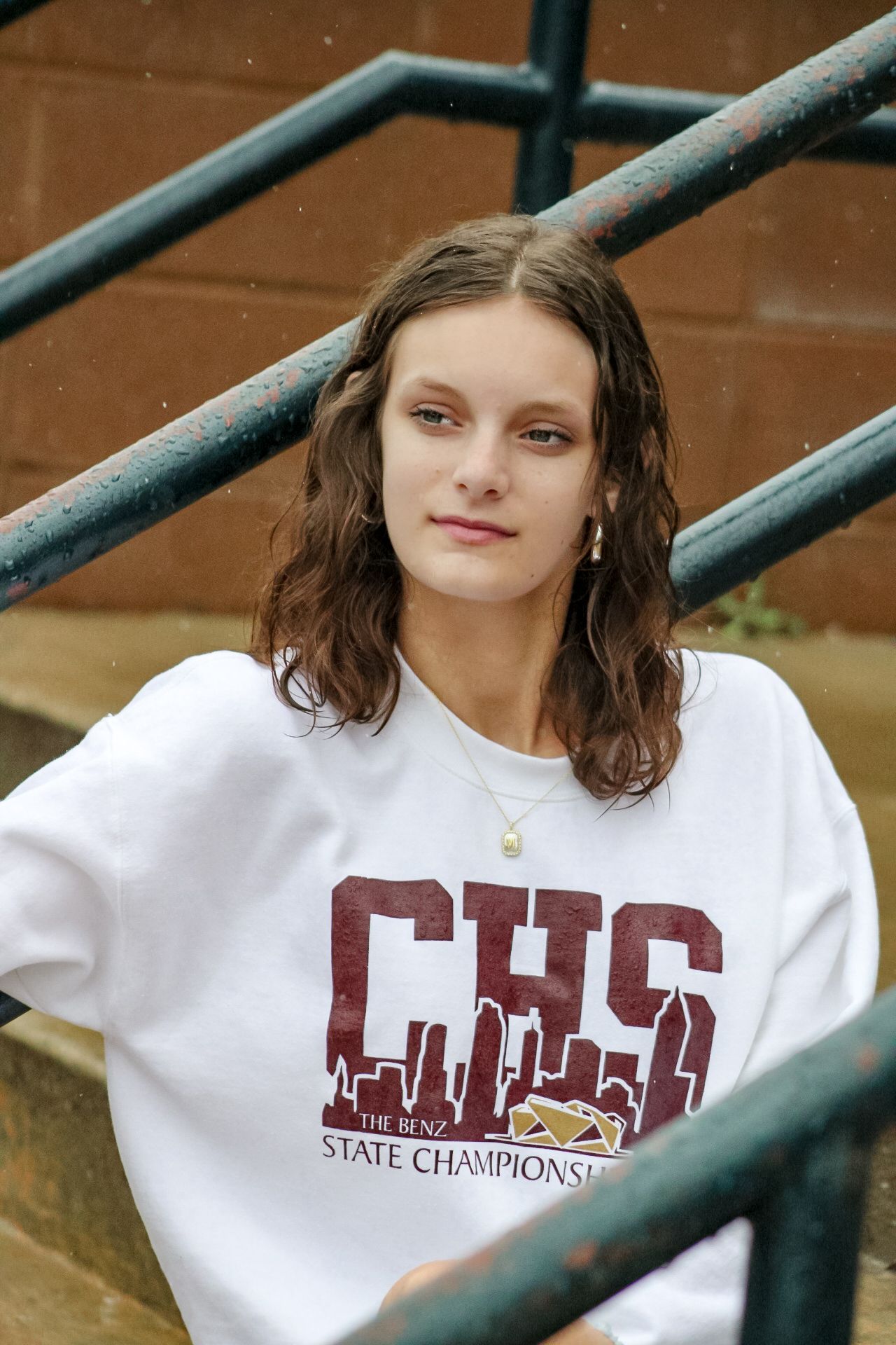 Young woman wearing a white CHS State Champions graphic t-shirt, posing on outdoor stairs with metal railings.