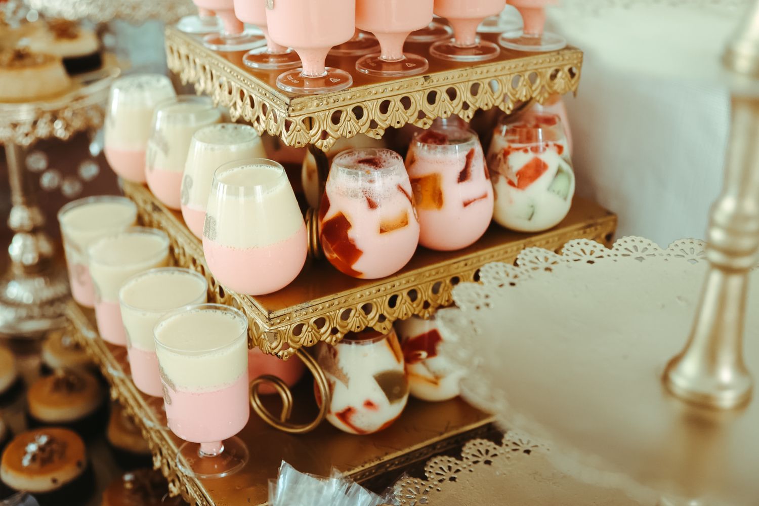 Elegant gold tiered dessert stand displaying pink and marble swirled mousse cups at a wedding reception.