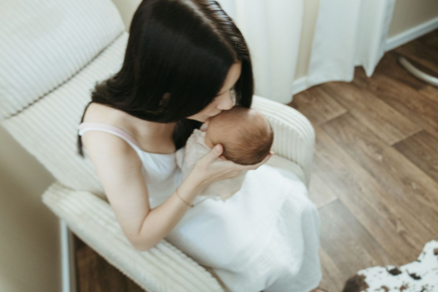 A woman in a white dress sits on a wooden floor holding a small white dog in her lap.