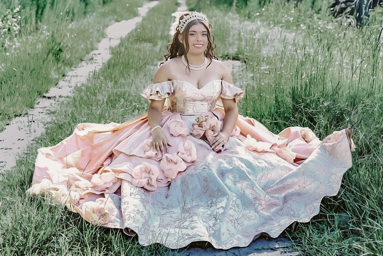 Woman in elegant pink ballgown sitting in grassy field wearing floral crown for a fairytale photoshoot.