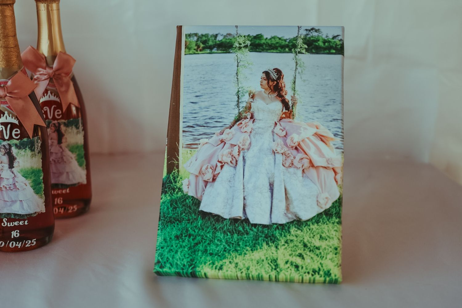 A quinceañera photo print displayed on a table beside decorated champagne bottles at a celebration.