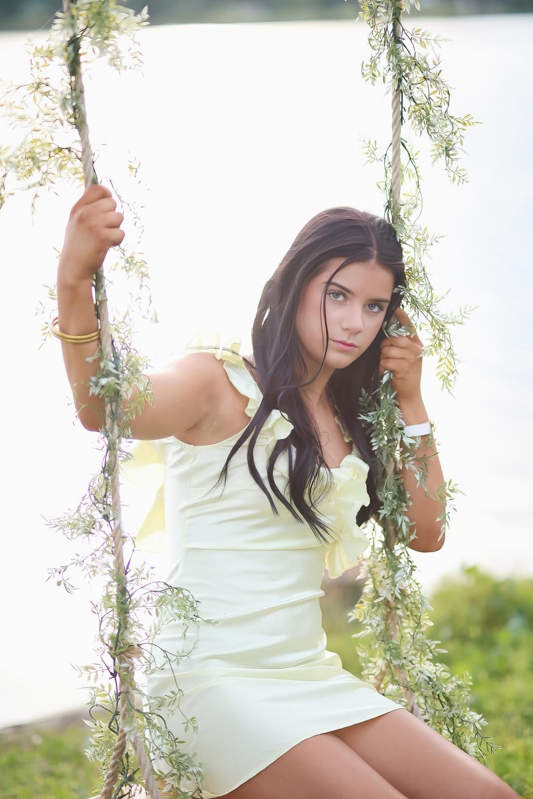 A white sundress adorns someone posing gracefully on a vine-covered garden swing with soft natural lighting.