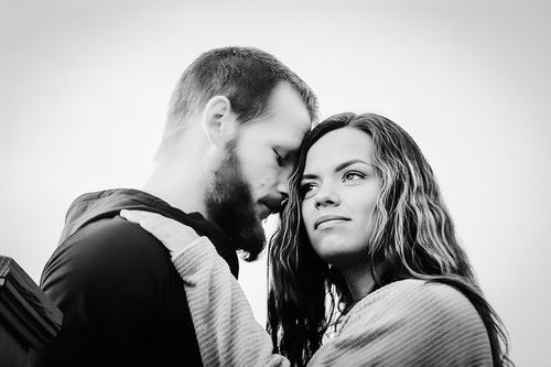 Black and white photo of a bearded man and curly-haired woman sharing an intimate moment outdoors.