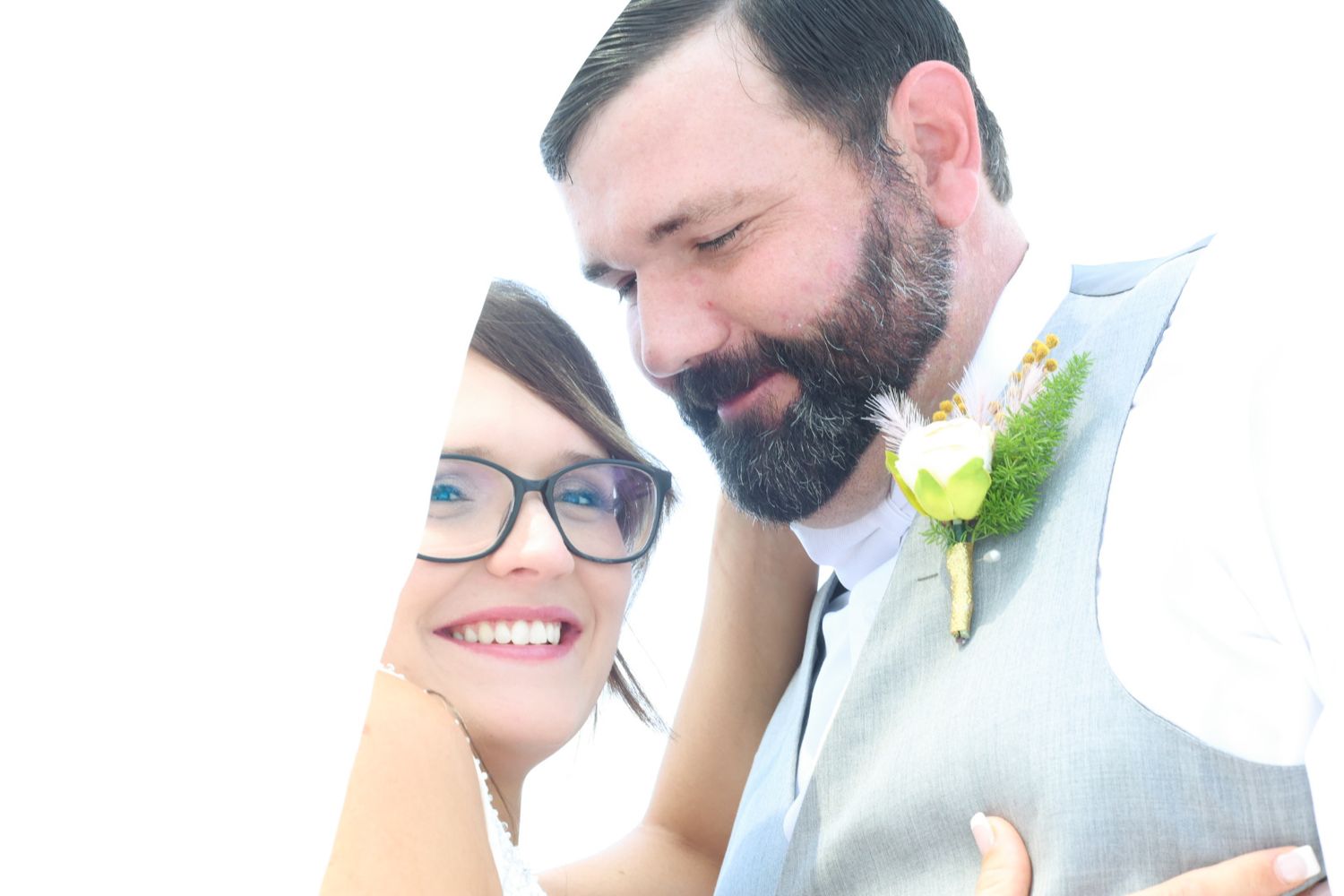 A happy couple shares a tender moment on their wedding day, with the groom wearing a light blue vest and floral boutonniere.