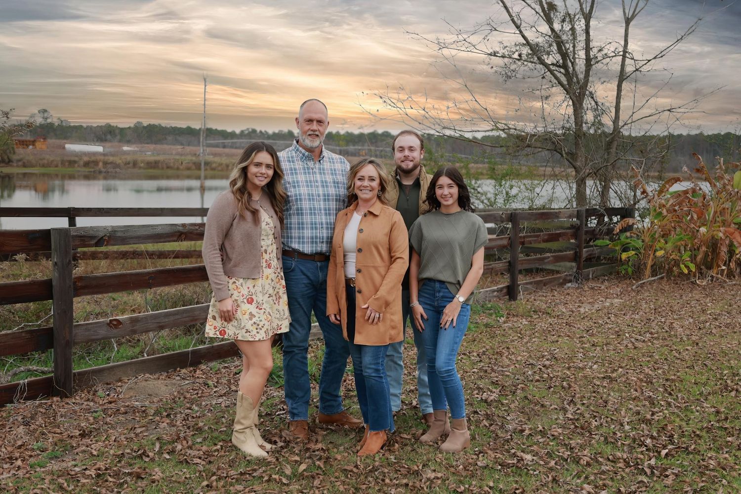 Group photo taken outdoors against a scenic autumn backdrop with wooden fence and fall foliage.
