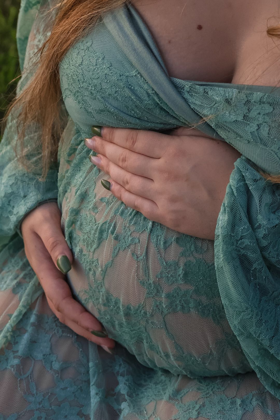 Close-up view of hands resting on a turquoise lace dress showing delicate fabric details and texture.