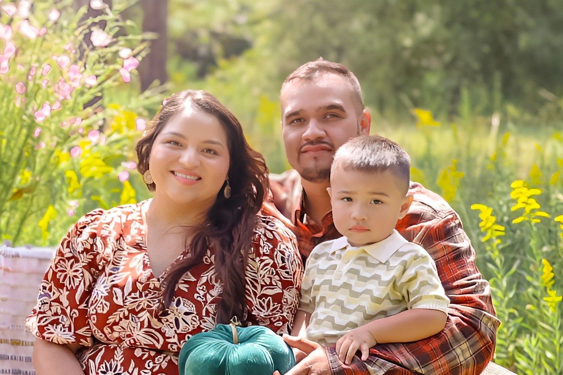 A family wearing matching red and white outfits poses together in a field of yellow wildflowers on a sunny day.