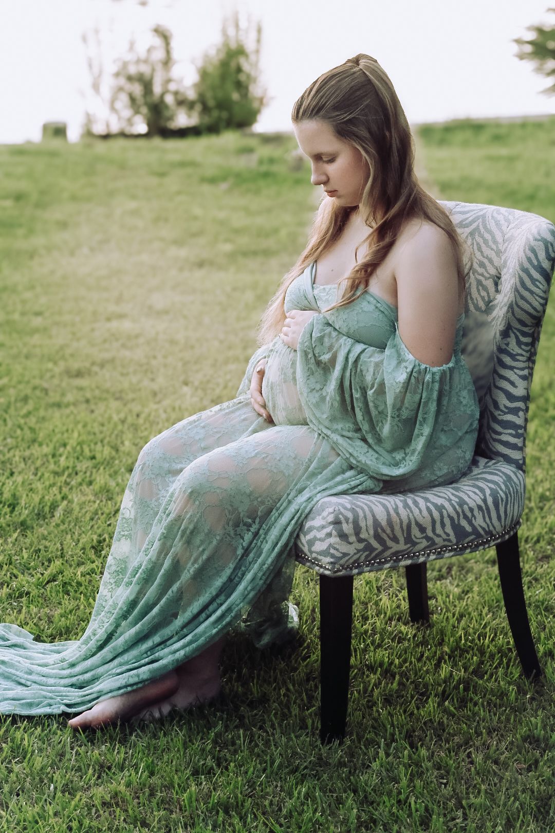 A maternity photo in an outdoor setting shows an expectant mother in a flowing mint green dress seated on a patterned chair.