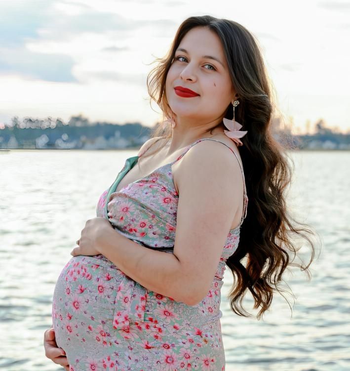 Woman in floral dress poses by waterfront during sunset, creating romantic coastal portraits.