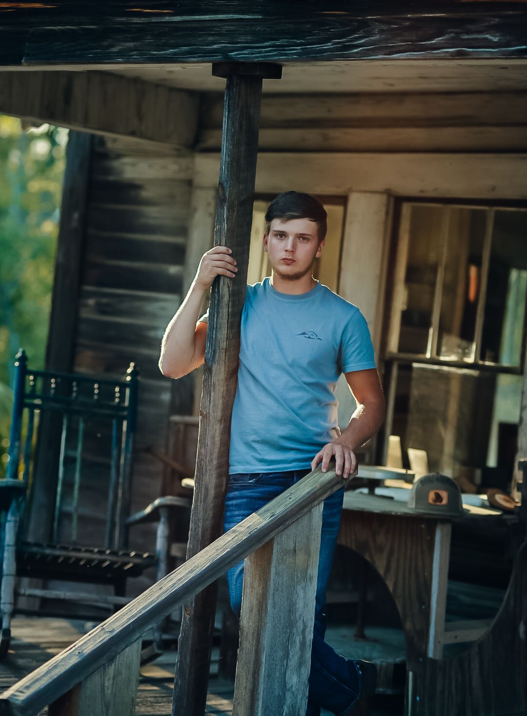 Person in blue t-shirt leans against wooden railing of rustic cabin porch.