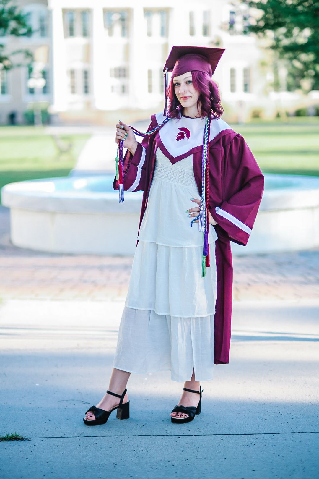 Graduation photos showing maroon cap and gown with white dress on concrete walkway.